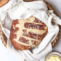 Warm challah bread with coarse salt in basket on white marble surface.
