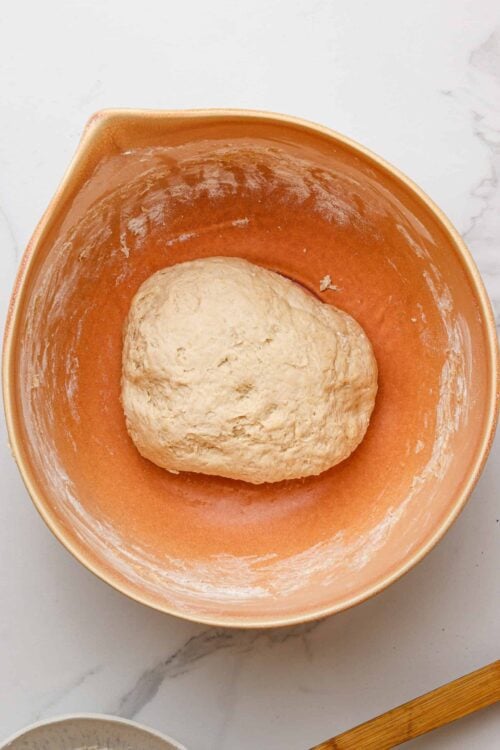 Soft bread dough resting in a peach-colored mixing bowl.