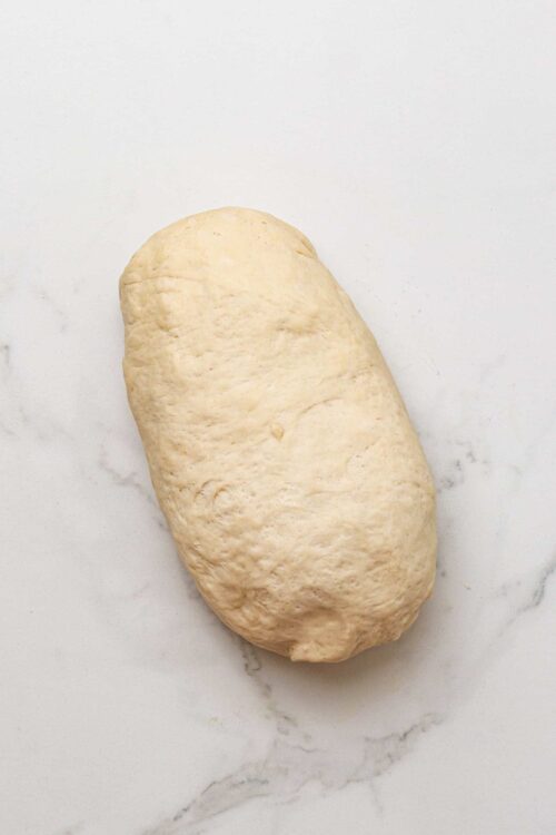 Dough ball for homemade bread or bakery recipes on white marble surface.
