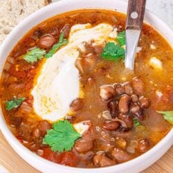 Hearty chili with beans in a white bowl garnished with cilantro and sour cream, served with bread.