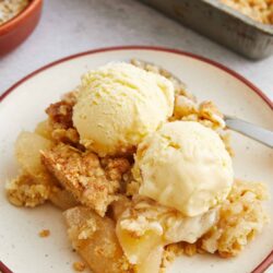 Warm apple crumble with vanilla ice cream on a white plate.