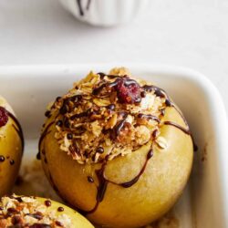 Sweet baked apples stuffed with granola and dried cherries, drizzled with chocolate, ready to serve.