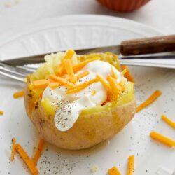 Baked potato topped with sour cream, shredded cheddar cheese, and black pepper.