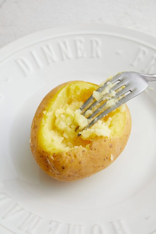 Baked potato with fluffy interior and crispy skin on a white plate.