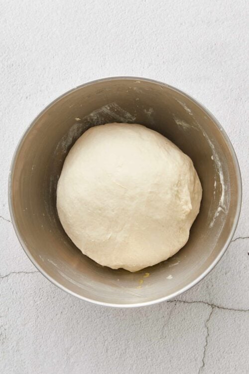 Soft dough resting in a stainless steel mixing bowl for baking bread or rolls.
