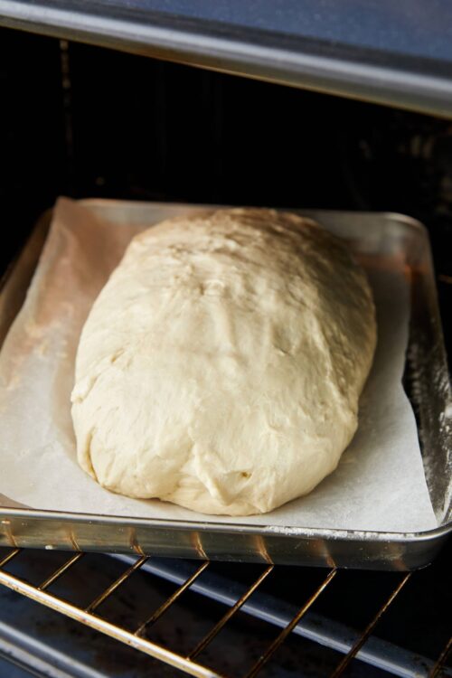 Soft bread dough rising in oven on parchment paper.