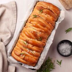 Buttery braided bread with rosemary garnishes on parchment paper.