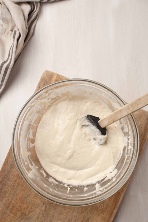 Creamy pancake batter in a glass mixing bowl on a wooden board.