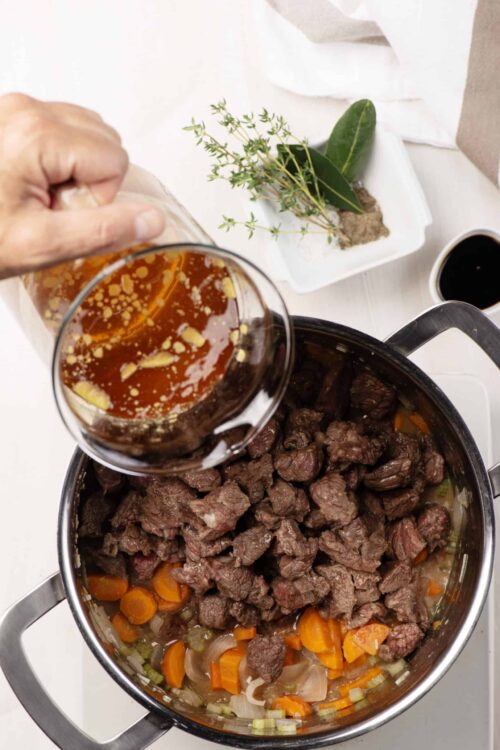 Tender beef stew with chopped carrots and onions cooking in an instant pot. Adding beef broth for rich flavor.