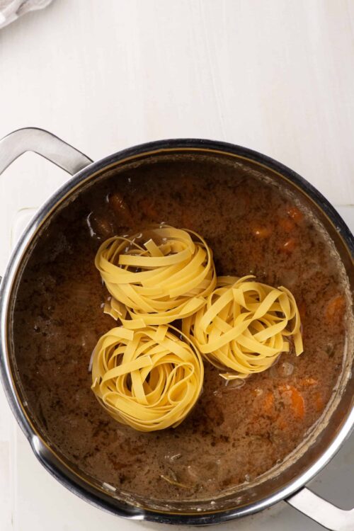 Cooked beef stew with pasta nests in a pot, ready to serve.