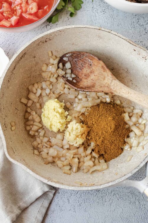 Creamy diced onions cooking with garlic and curry powder in a skillet for flavorful dish.