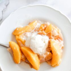 Sweet peach cobbler with vanilla ice cream on a white plate, perfect for summer desserts.