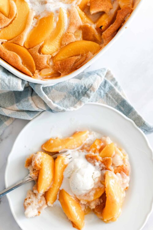 Peach cobbler baking dish with fresh peach cobbler served on a white plate with a scoop of vanilla ice cream, hot peach dessert, and crumb topping.