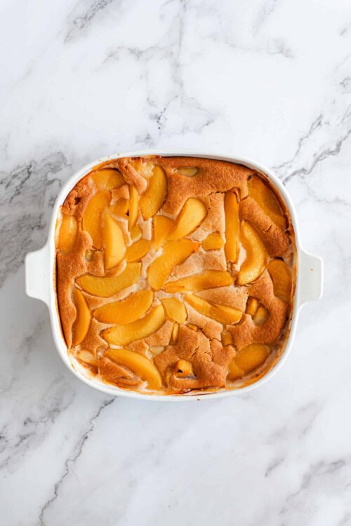 Sweet peach cobbler in a white baking dish on marble surface.