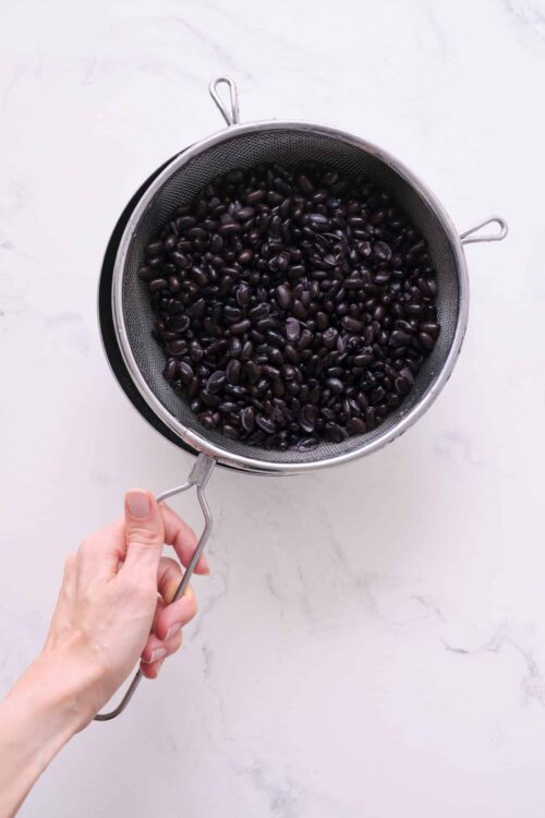 Juicing black beans in a metal strainer, healthy black beans for recipes, Baked Bree.