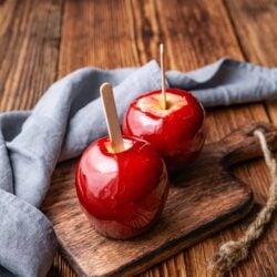 Sweet candied apples on wooden serving board with popsicle sticks.