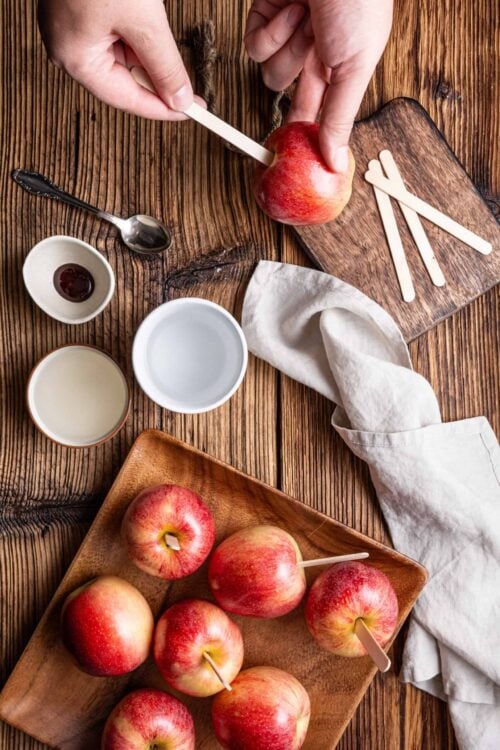 Fresh apples with popsicle sticks for caramel apple treats on rustic wooden table.