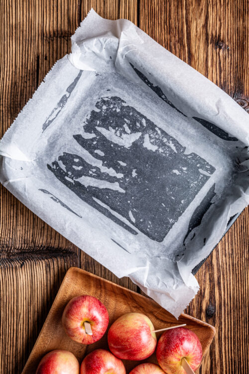 Baked Bree baking sheet with parchment paper, wooden table, and fresh apples for baking or roasting.