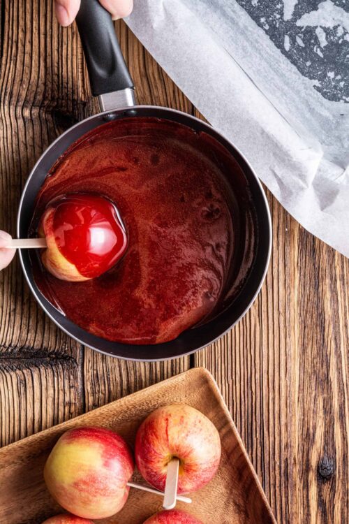 Sweet apple caramel dip in a saucepan with fresh apples on a wooden table.