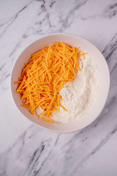 Shredded cheddar cheese on flour in a mixing bowl for baking recipes.