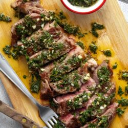 Juicy grilled steak topped with fresh chimichurri sauce on a wooden cutting board. Perfect for summer barbecue recipes.
