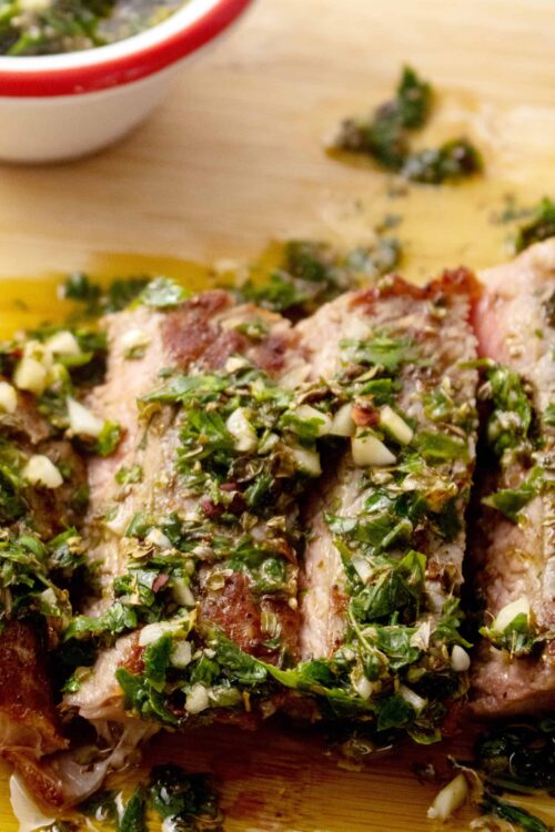 Juicy herb-marinated pork tenderloin garnished with chopped garlic and herbs on a wooden cutting board.