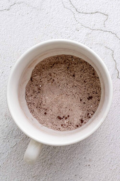 Fine cocoa powder in a white mug on textured white surface, baking ingredients, cocoa for desserts.