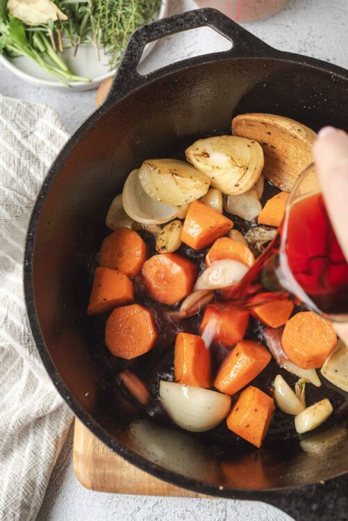 Sweet roasted vegetables including carrots, onions, and garlic in a cast iron skillet.