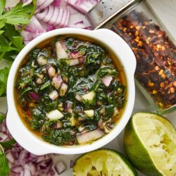 Fresh apple and chili pepper salsa with lime, garnished with herbs, on a white plate.