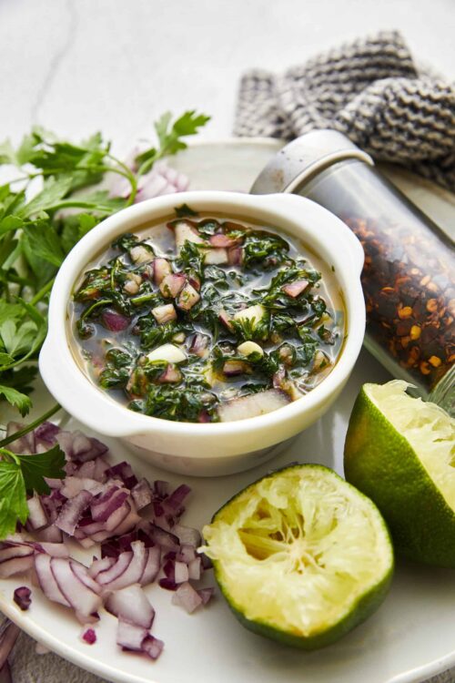 Fresh homemade salsa with chopped onions, cilantro, and lime on a rustic white plate.