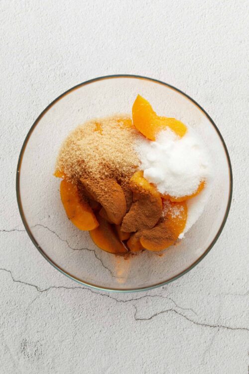 Fresh peach cobbler ingredients in a glass bowl for baking, showcasing homemade dessert preparation.