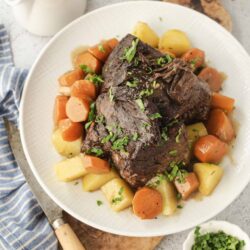 Braised beef short ribs with vegetables on a white plate, rustic home-cooked comfort food.