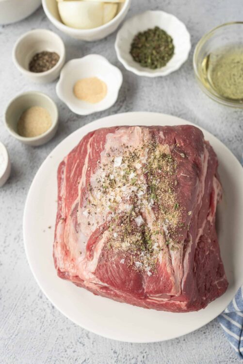 Seasoned raw beef roast with herbs and spices on a white plate.