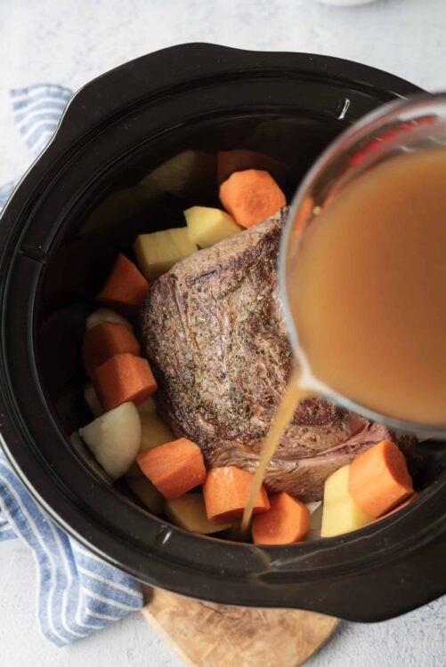 Slow cooker beef stew with carrots, potatoes, and broth in a black crockpot.