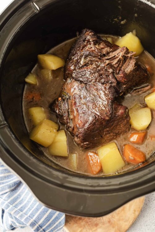 Juicy pot roast with vegetables cooking in a slow cooker.