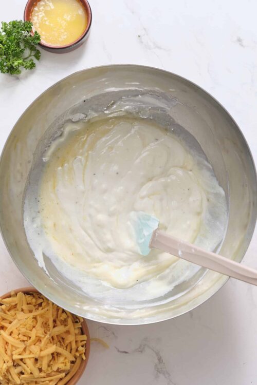 Creamy cheese sauce mixture in stainless steel bowl for baked pasta or casserole dish.