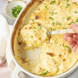 Creamy cheesy baked chicken and potato casserole in a white ceramic dish garnished with fresh herbs.