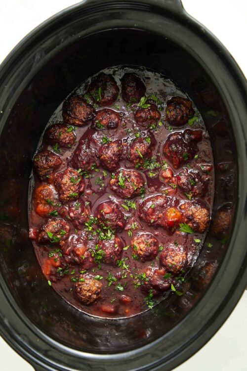 Savory meatballs in slow cooker with tomato sauce and herbs.