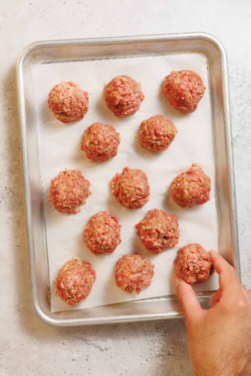 Seasoned raw meatballs on baking sheet for baking or cooking.