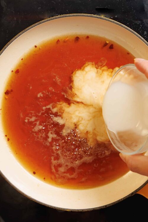 Cream being poured into flavorful broth with spices in a skillet.