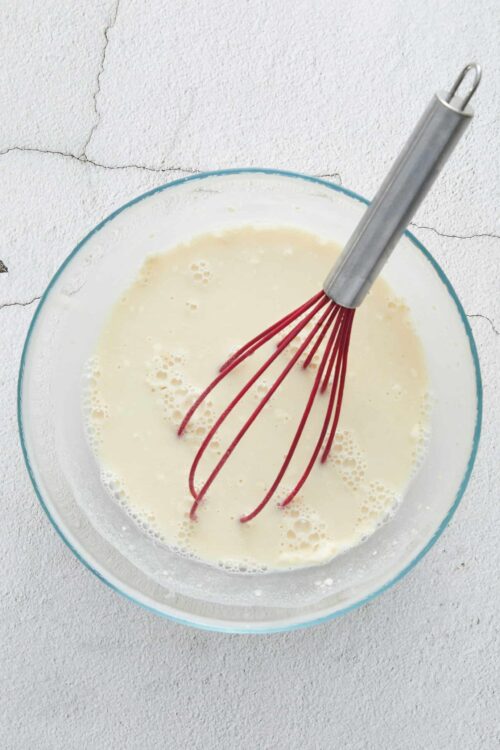 Whisk with batter in glass bowl, baking ingredients, and kitchen cooking process for baked goods.