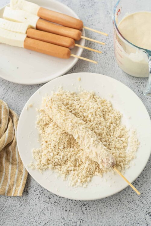 Raw chicken skewers breaded with panko crumbs on a white plate.