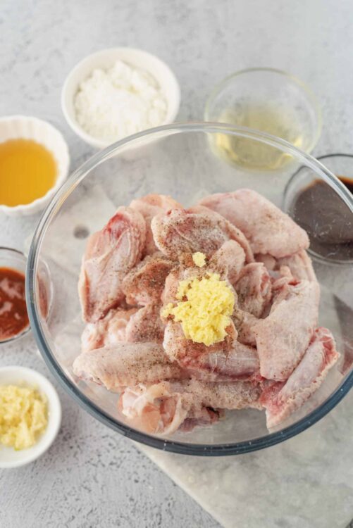 Raw chicken pieces with seasonings and butter in a glass bowl for baking or cooking.