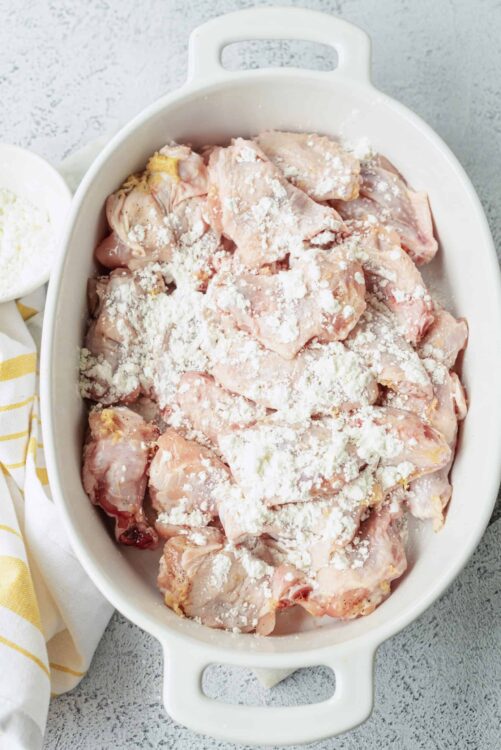 Raw chicken pieces coated with flour in a white baking dish.