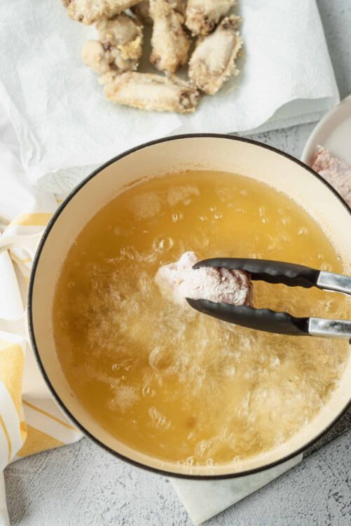 Crispy fried chicken being dipped into hot oil in a skillet for perfect golden brown coating.