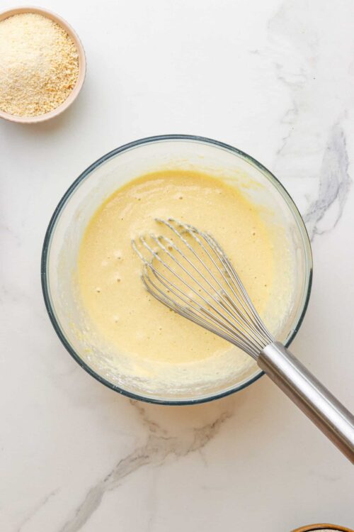 Fluffy cake batter in a glass mixing bowl with a whisk, ready for baking.