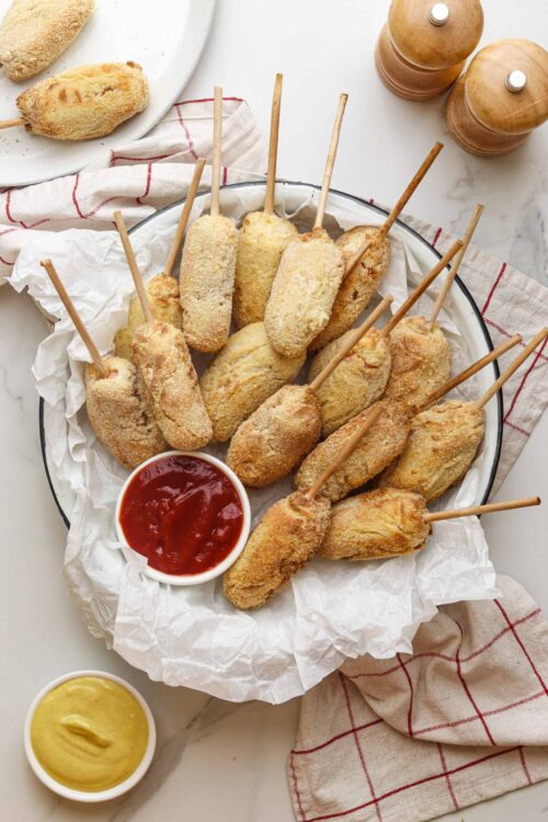 Crispy baked chicken drumsticks on skewers with dipping sauces on a white plate.