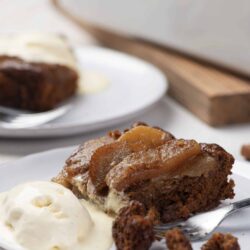 Decadent apple spice cake with caramelized apple topping and vanilla ice cream on white plate.