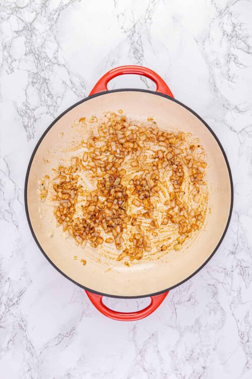 Sautéed onions in a red cast iron skillet for cooking or recipe preparation.