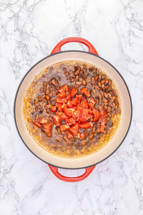 Cooked black beans with chopped tomatoes in a red cast iron skillet, ready for a savory dish.